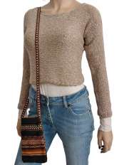 Sobre fondo blanco, mujer con jersey corto beige en baby alpaca y algodón Pima, modelo Fiona, jeans y portamóvil étnico peruano.