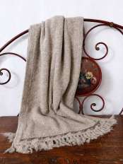 Chal bufanda beige de lana de alpaca con flecos, apoyado en una cabecera de cama de hierro sobre madera antigua, modelo Kora.